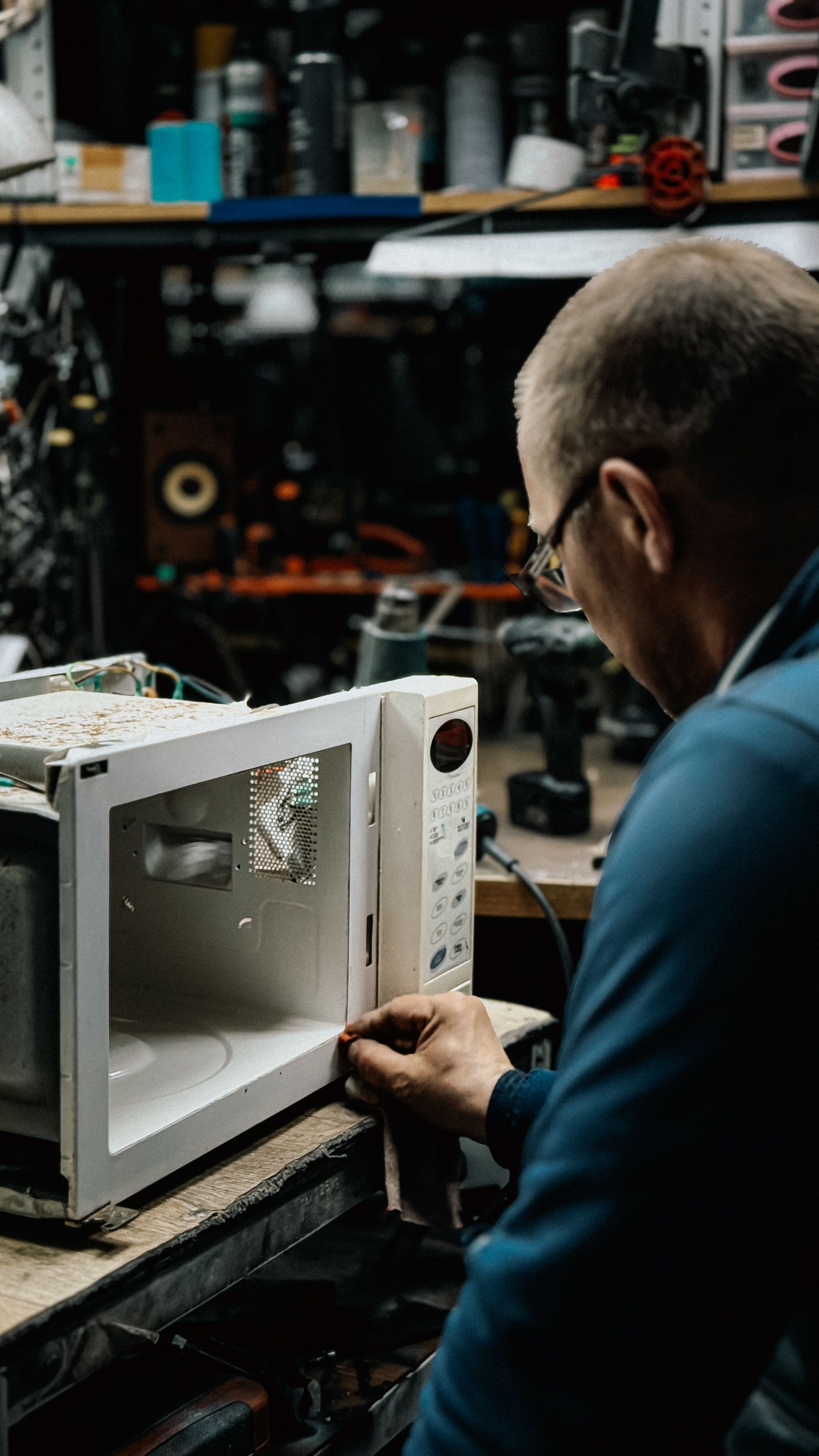 A technician examines an open microwave at a workbench in a small appliance repair shop